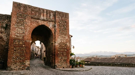 Porte fortifiee medievale en brique rouge et galets, vue en contre-plongee, symbolisant la strategie urbaine de Perpignan